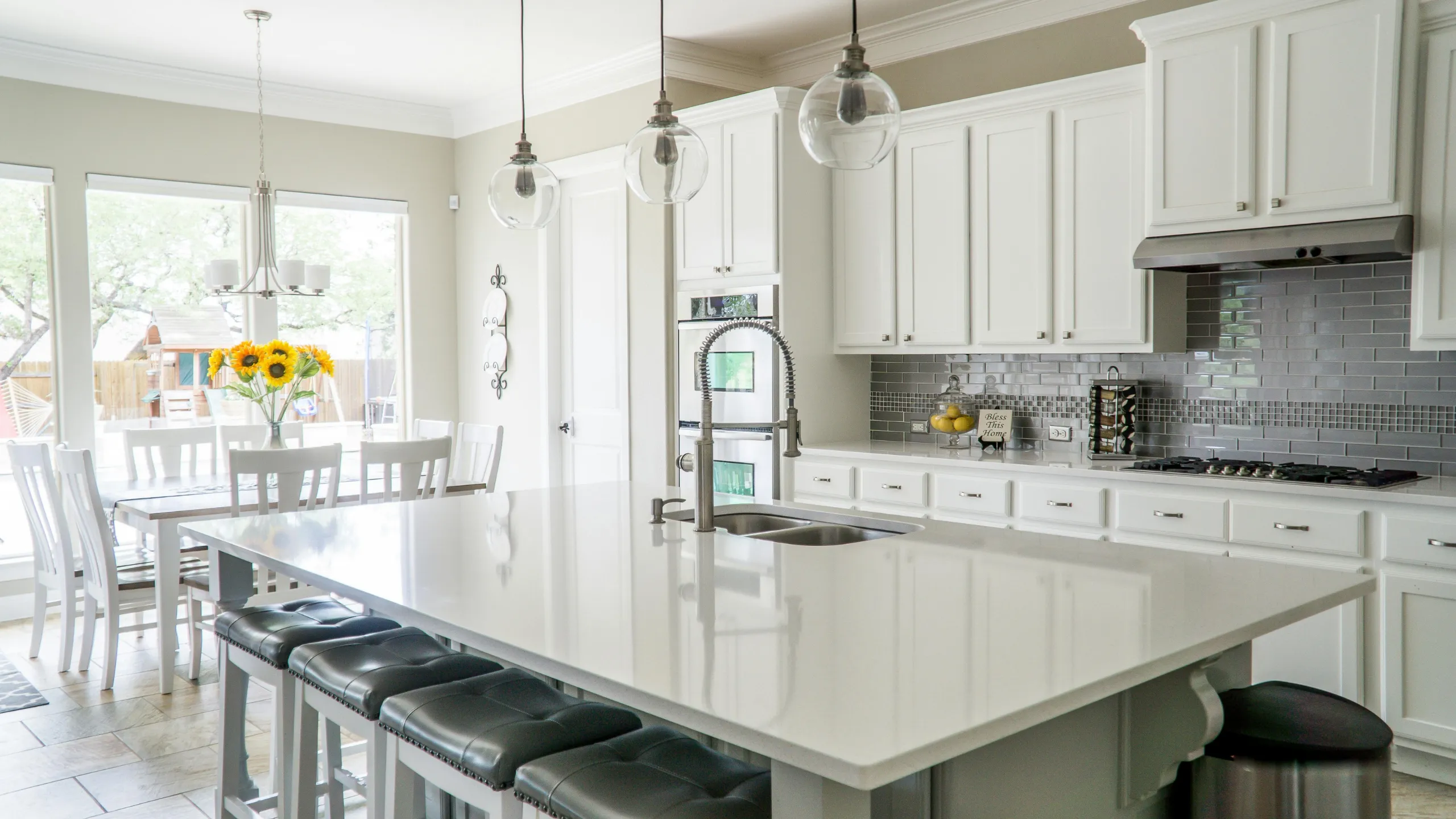 Fully restored modern kitchen featuring white cabinets, polished quartz countertops, gray subway tile backsplash, and a large island following emergency damage restoration.